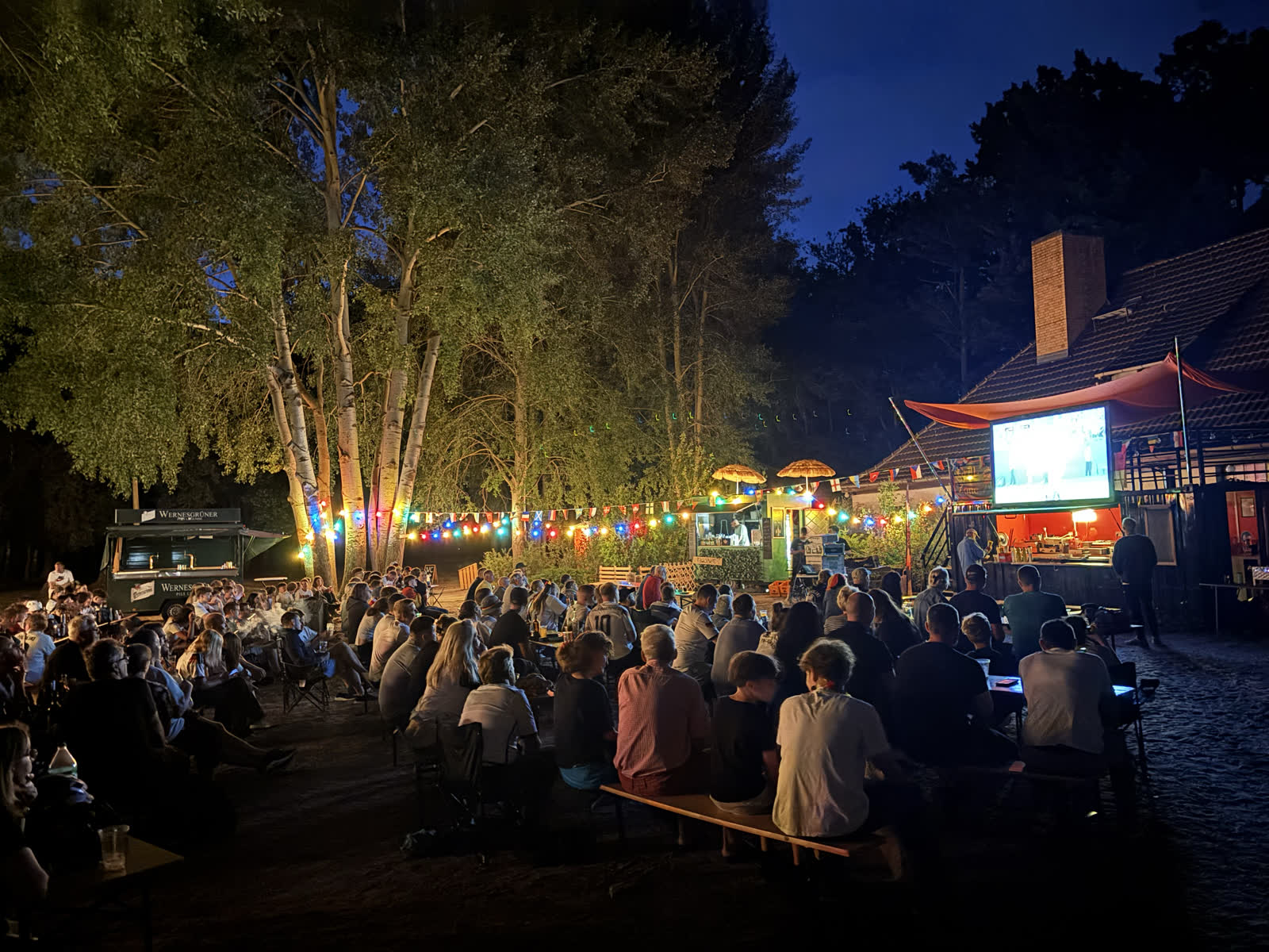 Gäste am Abend am Rangsdorfer See vor der Leinwand im Strandbad