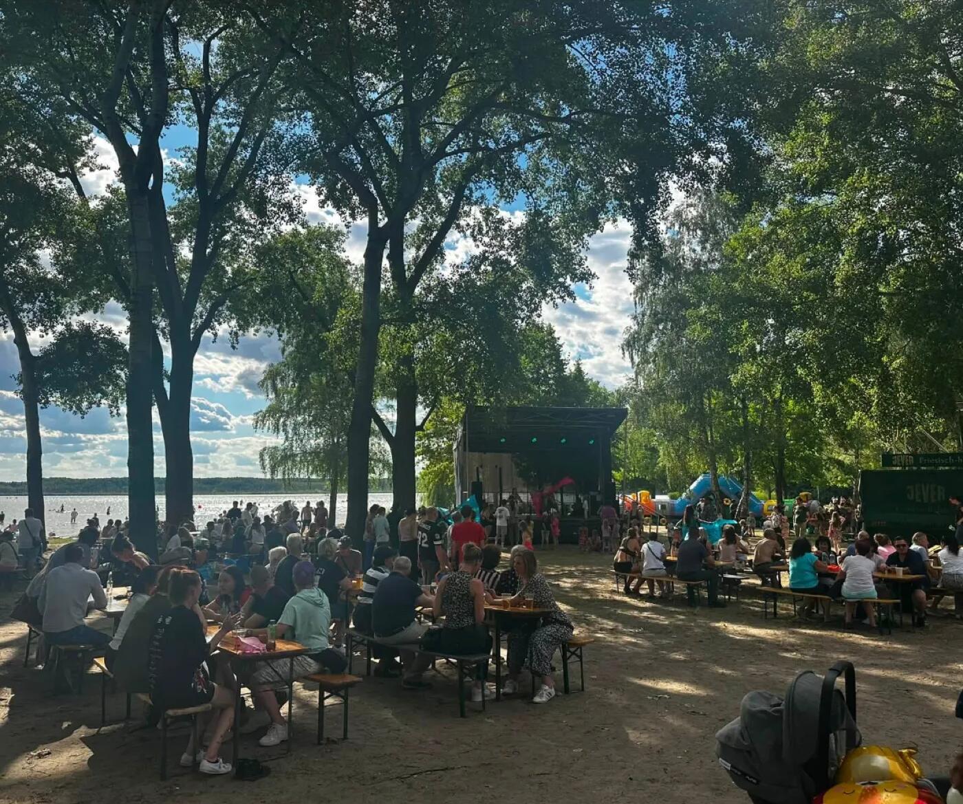 Gäste an Biertischen am Ufer des Rangsdorfer Sees während eines Sommerfests im Strandbad